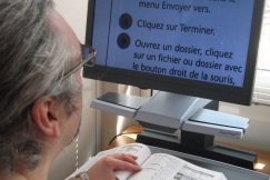 Un homme utilise un télé agrandisseur pour lire en gros caractères un document