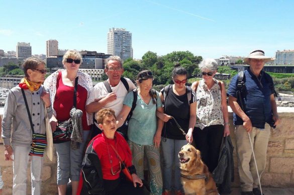 Groupes de bénéficiaires apputé sur une murette avec la ville en fond et le chien au premier plan. 