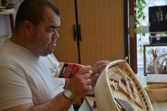 Un bénéficiaire tient une maquette de bateau en bois entre les mains et met une sorte de colle dessus pour combler les petits défauts. 