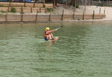 Casque jaune, planche au pied, le sportif tiend le palonnier et sort de l'eau.