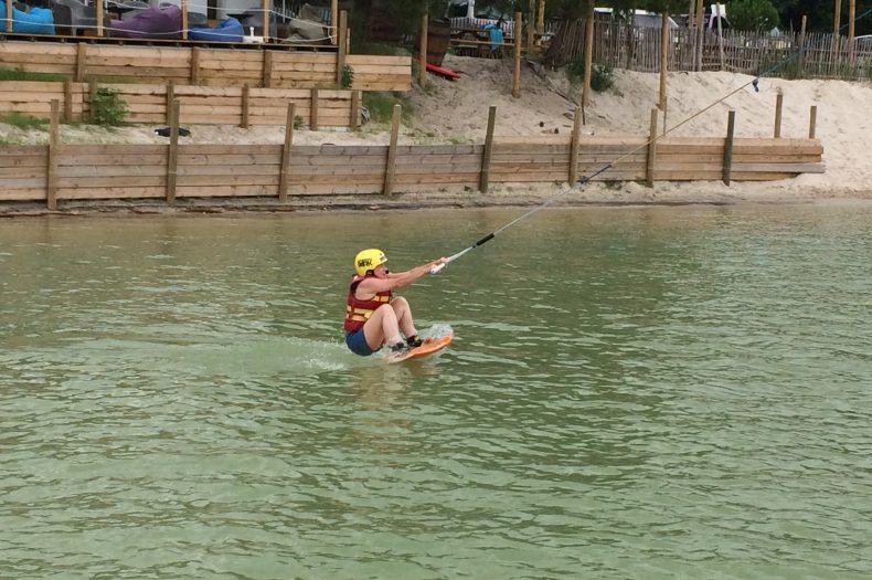 Casque jaune, planche au pied, le sportif tiend le palonnier et sort de l'eau. 