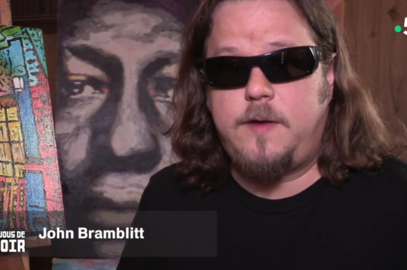 John Bramblitt avec des lunettes noires devant un portrait