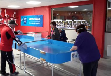 table de ping pong aux bords relevés dame qui joue avec une sorte de raquette.