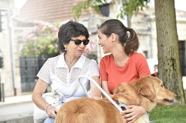 Une auxiliaire de vie assise sur un banc avec une personne aveugle accompagnée de son chien-guide