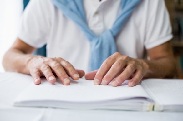 Un homme aveugle pose ses mains sur un livre transcrit en braille