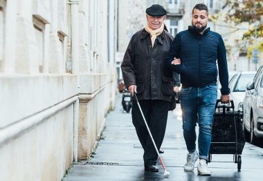 Florian, auxiliaire de vie, accompagne en ville Barthélémy-Michel, aveugle.